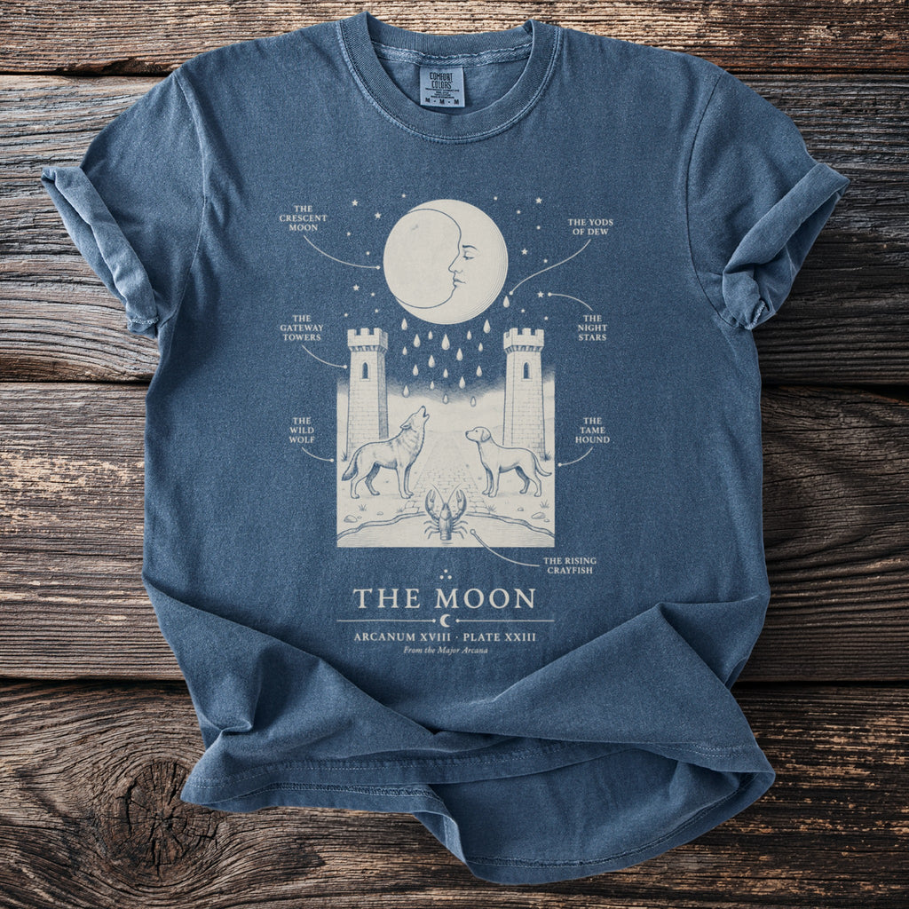 Blue t-shirt with "The Moon" tarot card art featuring a crescent moon, towers, wolf, dog, and crayfish.