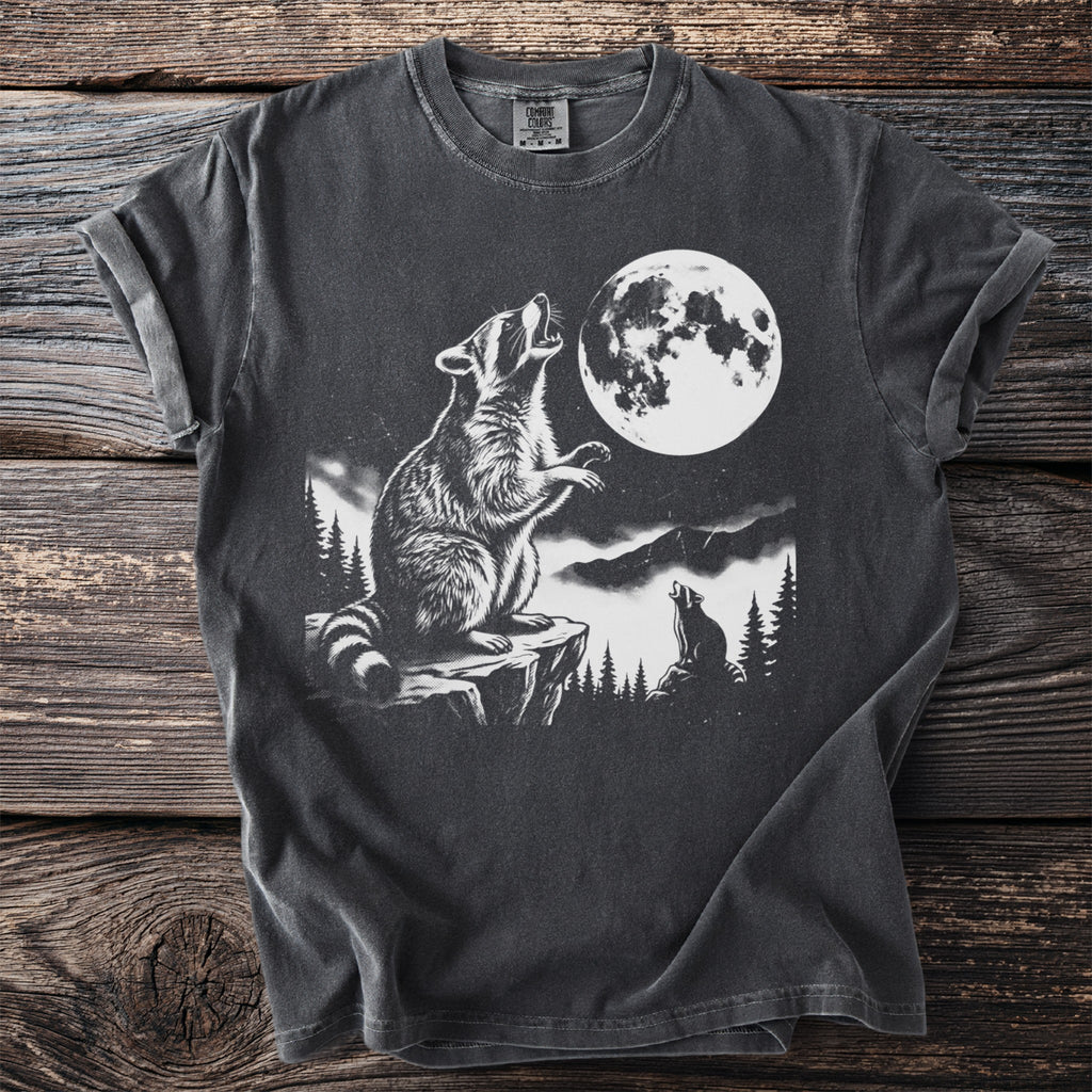 Graphic t-shirt with raccoon howling at full moon in mountainous forest scene.