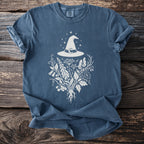 Blue t-shirt with white witch hat, crescent moon, and botanical illustration graphic.