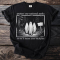 Black t-shirt with ghosts in a forest and text "protect our national parks or we'll haunt your backyard".