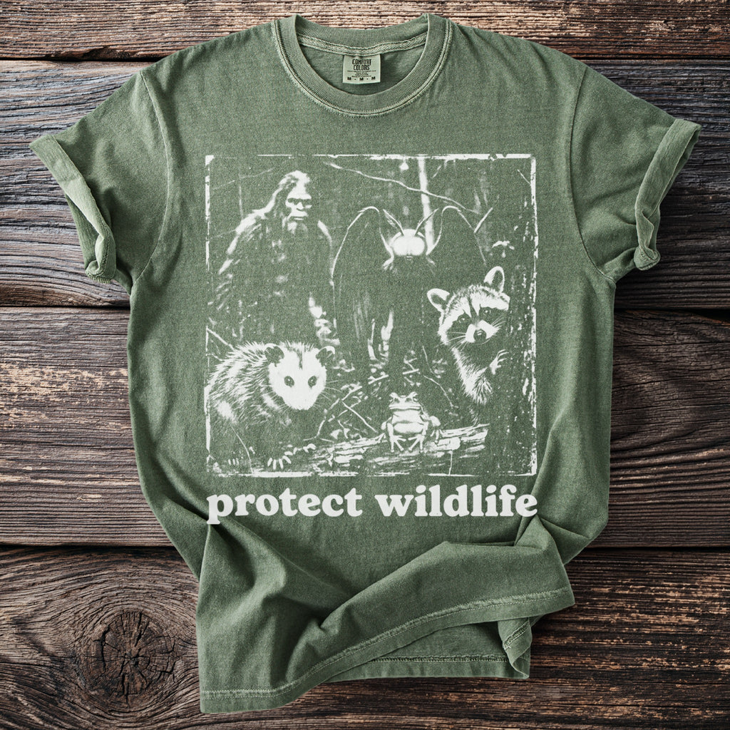 Green t-shirt with graphic of Bigfoot, bat, opossum, raccoon, and frog, saying "protect wildlife".