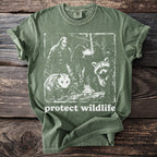 Green t-shirt with graphic of Bigfoot, bat, opossum, raccoon, and frog, saying "protect wildlife".