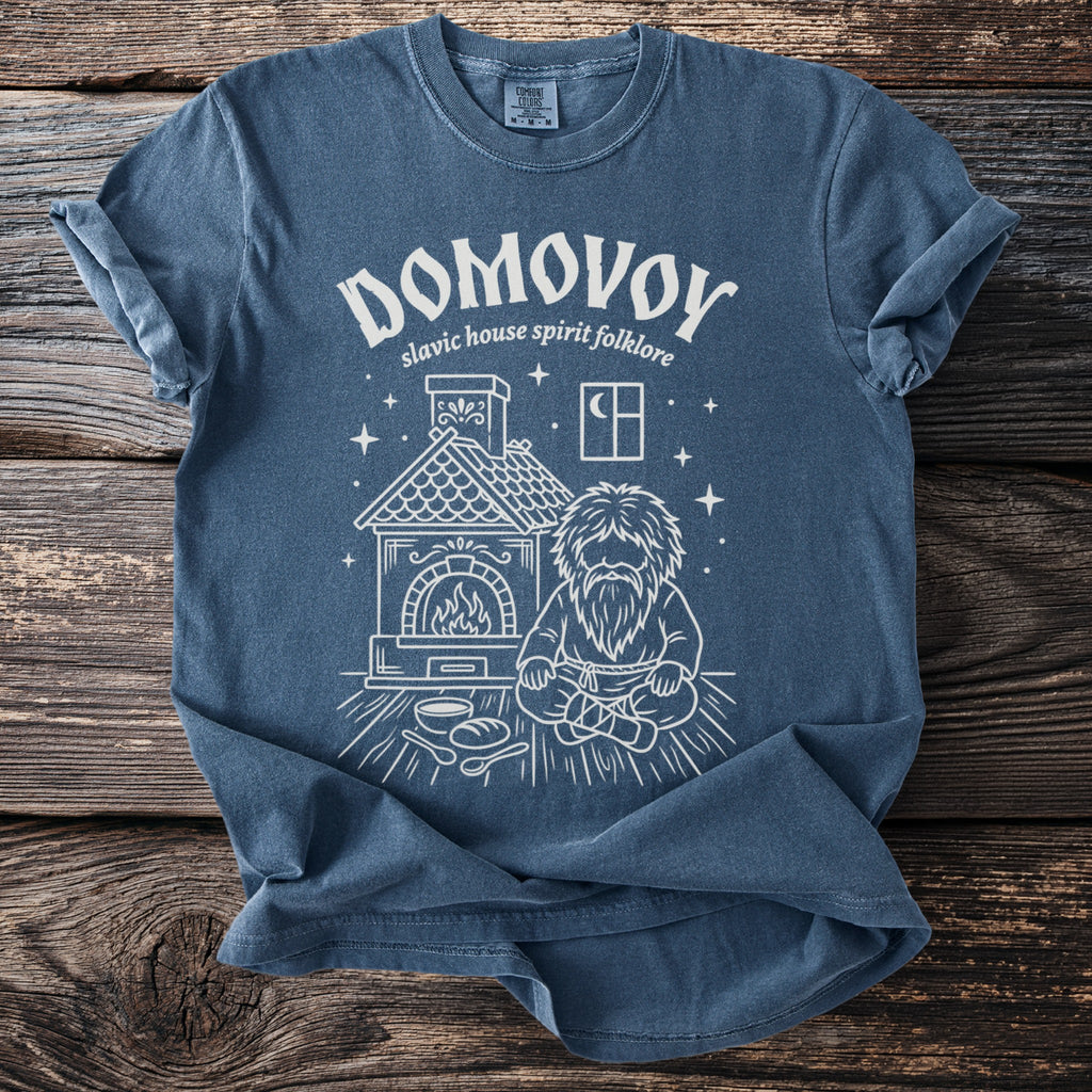 Blue t-shirt with white graphic of Domovoy, a Slavic house spirit, beside a hearth.