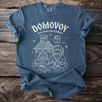 Blue t-shirt with white graphic of Domovoy, a Slavic house spirit, beside a hearth.