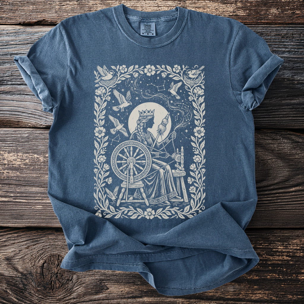 Blue t-shirt with a vintage queen spinning yarn at a wheel, surrounded by birds and constellations.