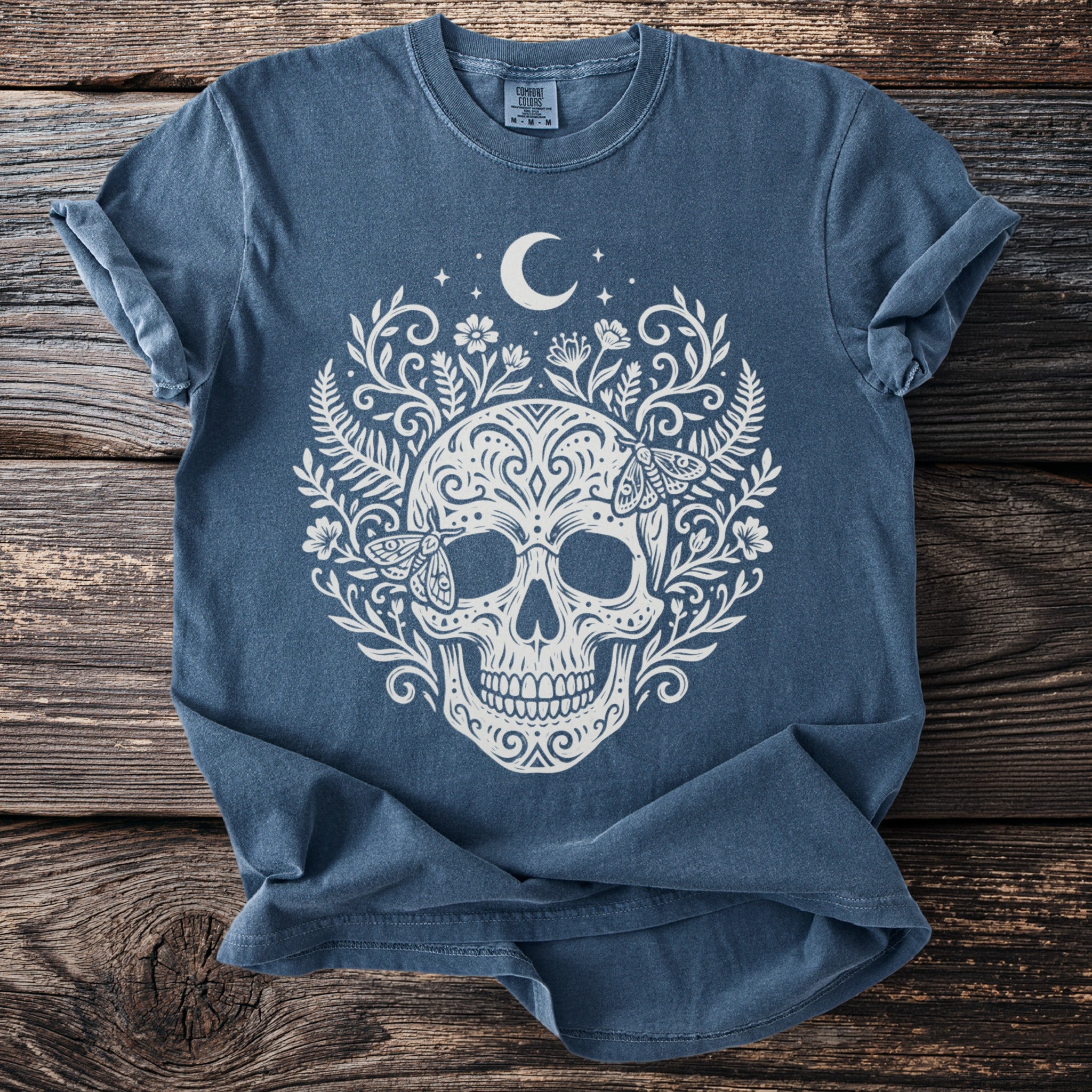 Blue t-shirt with white skull, floral, moth, and moon design.