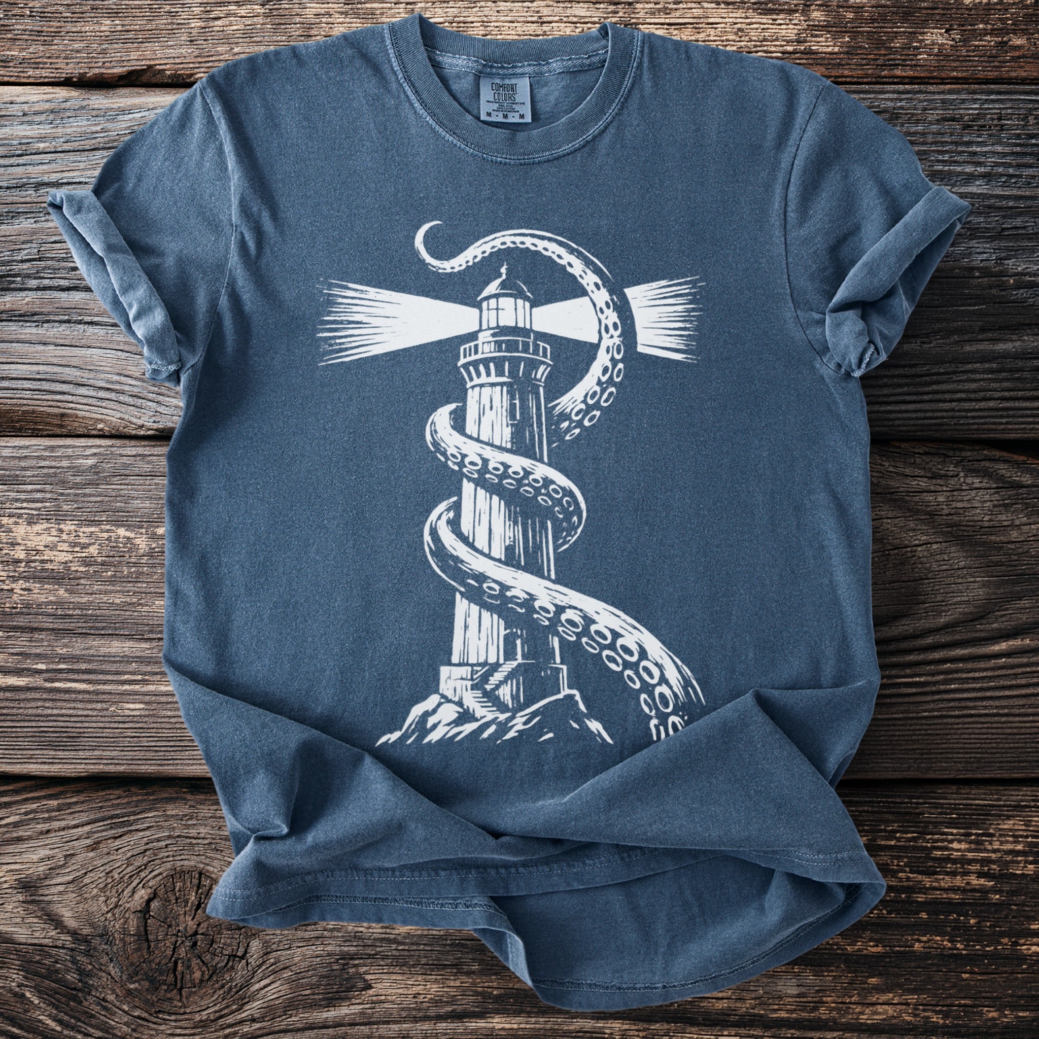 White graphic of a lighthouse entangled with an octopus tentacle on a blue t-shirt.