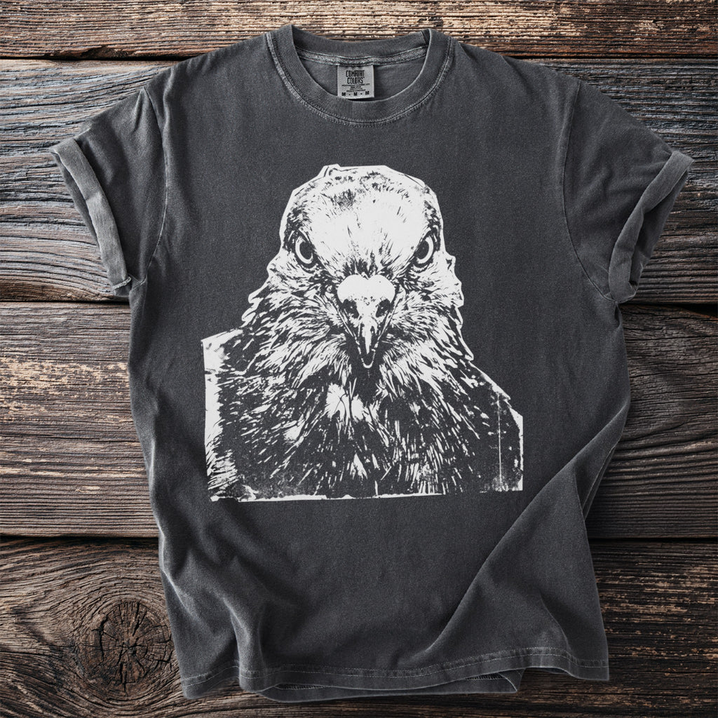 Dark t-shirt with a white close-up graphic of a pigeon's face staring straight ahead, on a wooden background.
