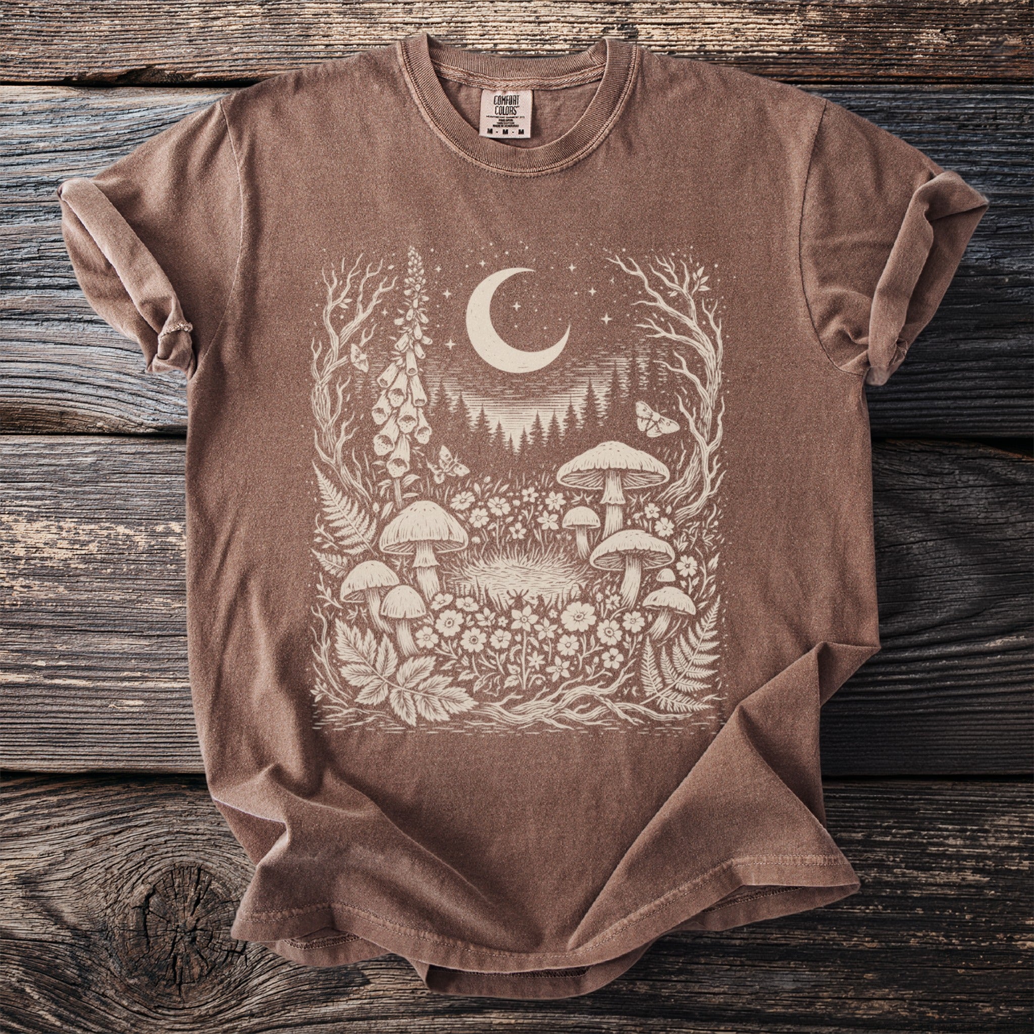 Brown t-shirt with an intricate cream graphic of mushrooms, flowers, a crescent moon, and stars.