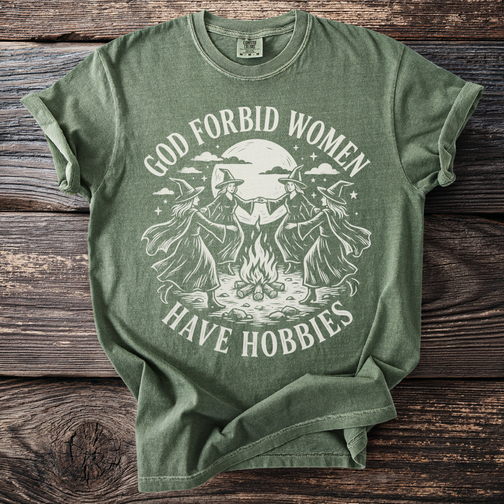 Green t-shirt with white graphic of witches dancing around a campfire under a moon.