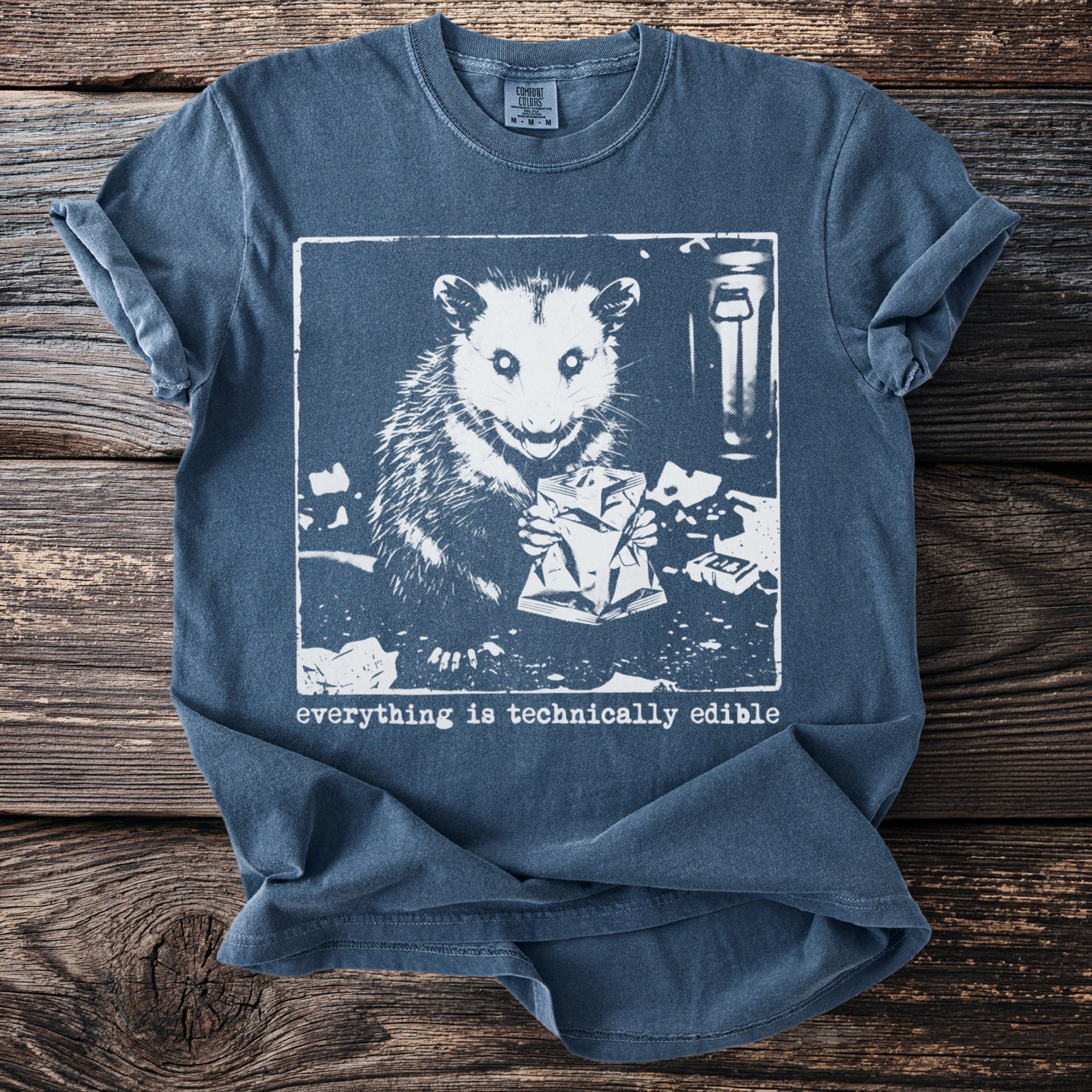 Opossum holding a bag of chips with the text "everything is technically edible."