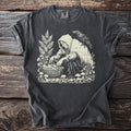 T-shirt with cream linocut print of a cloaked figure collecting mushrooms with a raven.