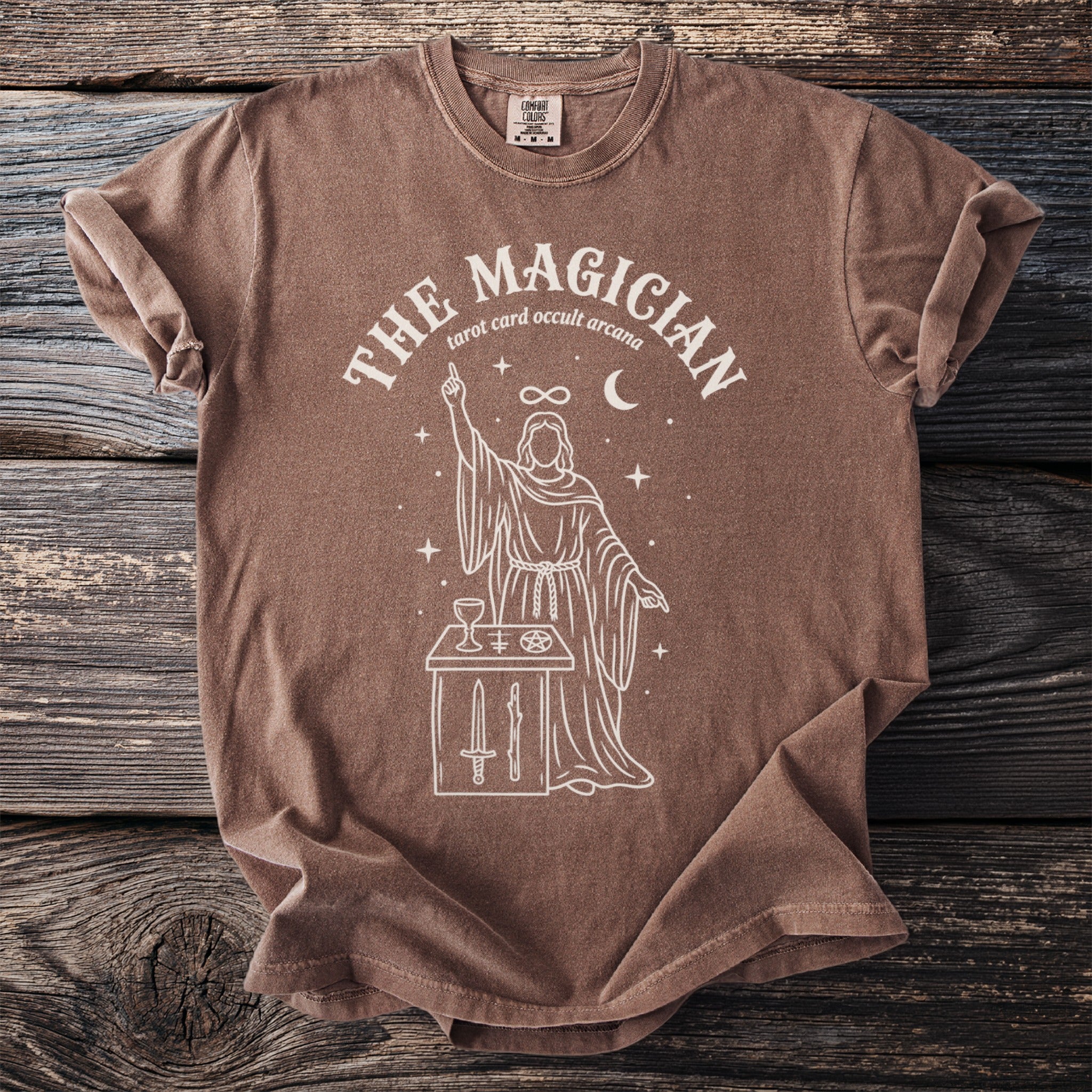 Brown t-shirt with white line art of "The Magician" tarot card and occult symbols.