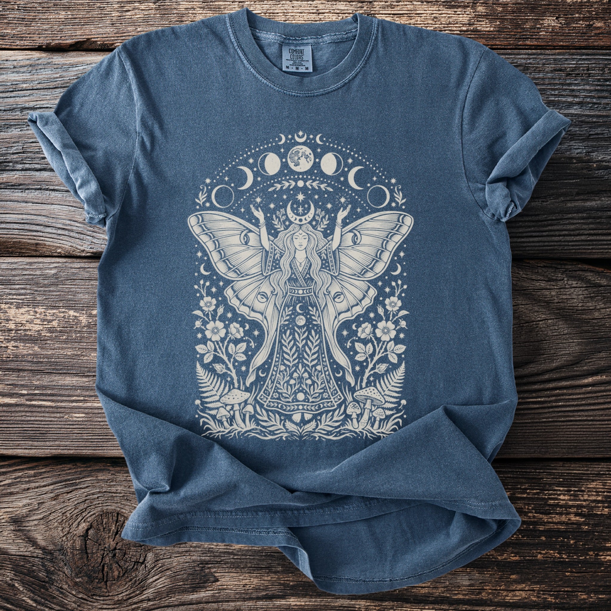 Blue t-shirt with moth fairy, mushrooms, flowers, and moon phase graphic design.