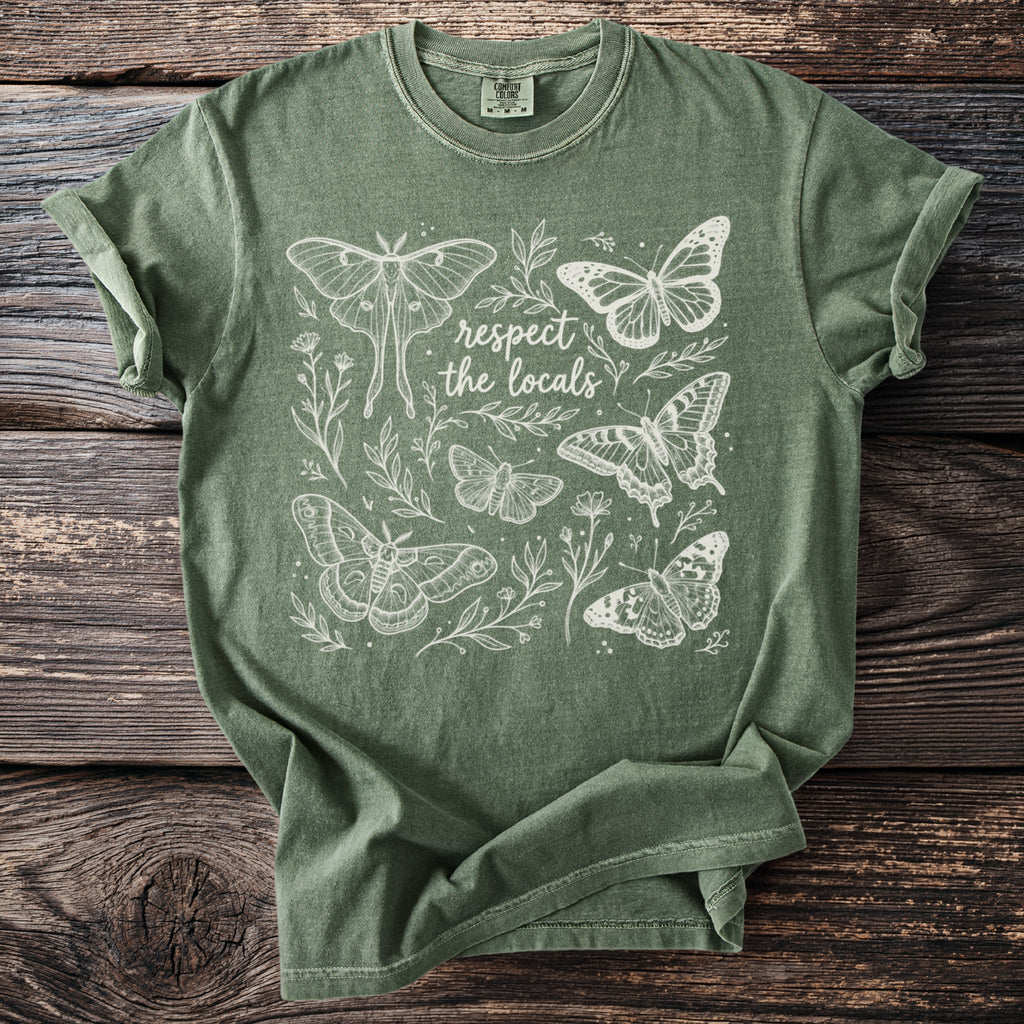 Green t-shirt with white line art of moths, butterflies, and text reading "respect the locals".