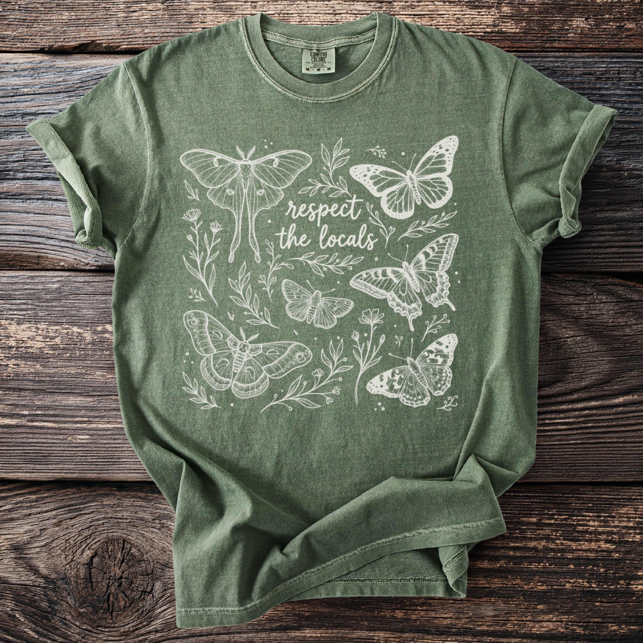 Green t-shirt with white line art of moths, butterflies, and text reading "respect the locals".