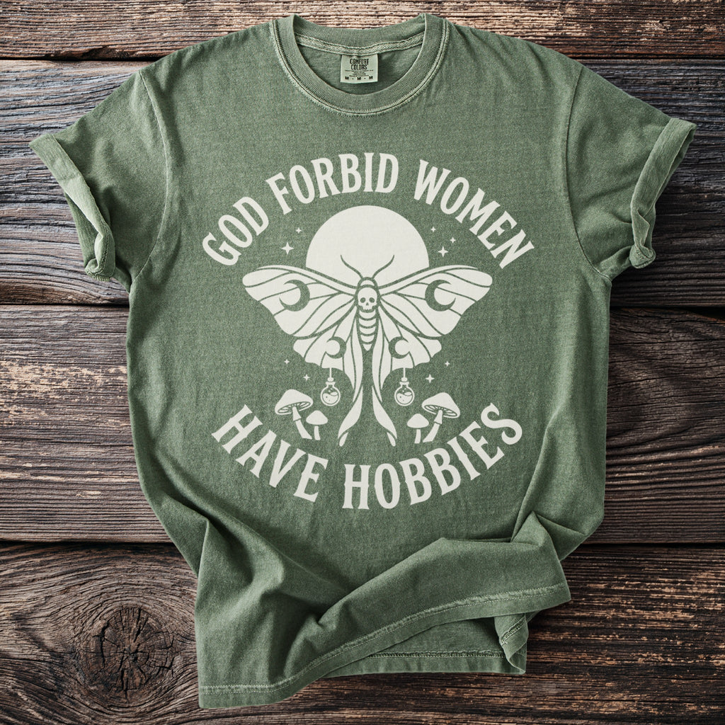 Green t-shirt with a moth, mushrooms, and text "GOD FORBID WOMEN HAVE HOBBIES".
