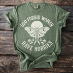 Green t-shirt with a moth, mushrooms, and text "GOD FORBID WOMEN HAVE HOBBIES".