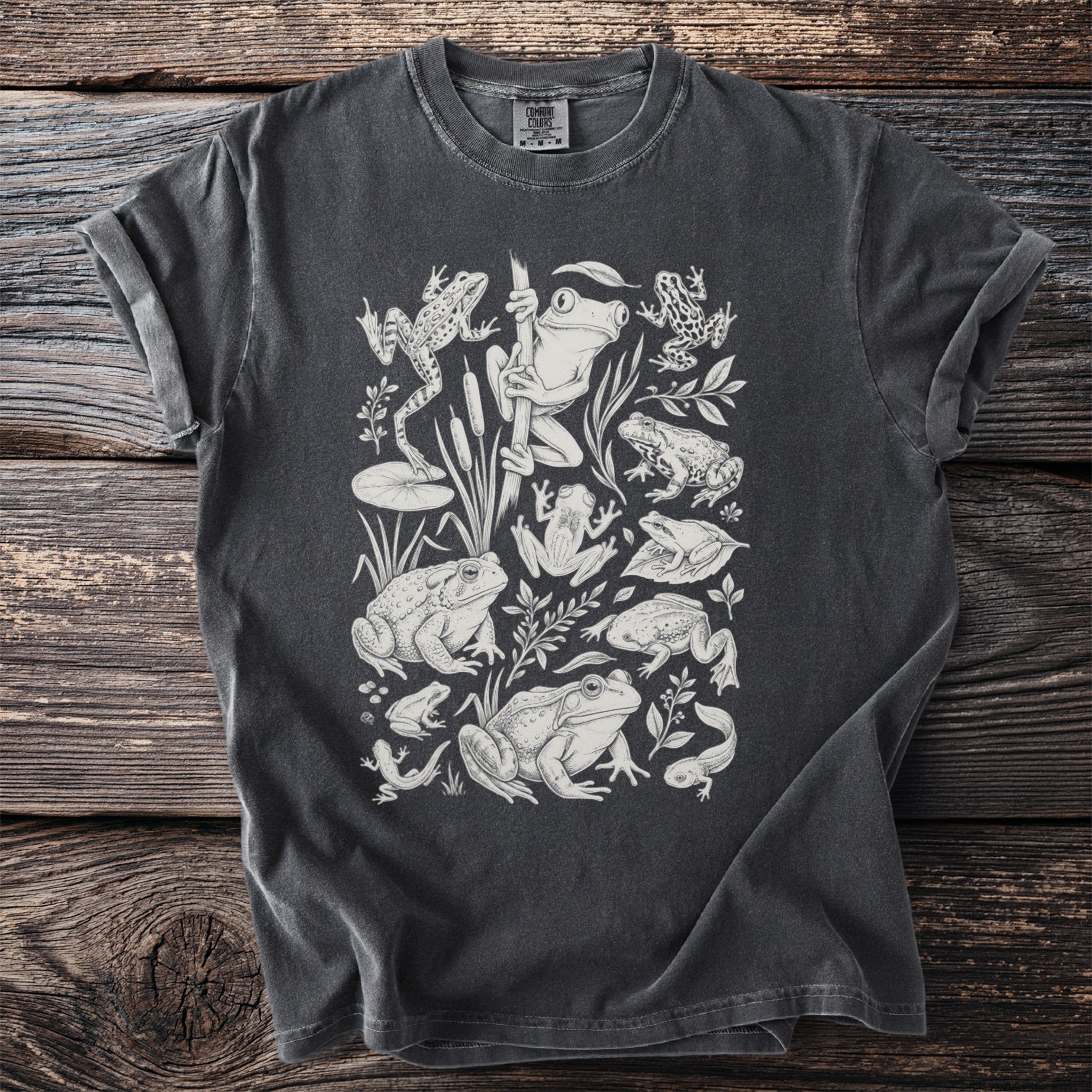 Dark gray t-shirt with a white linework print of various frogs and tadpoles.