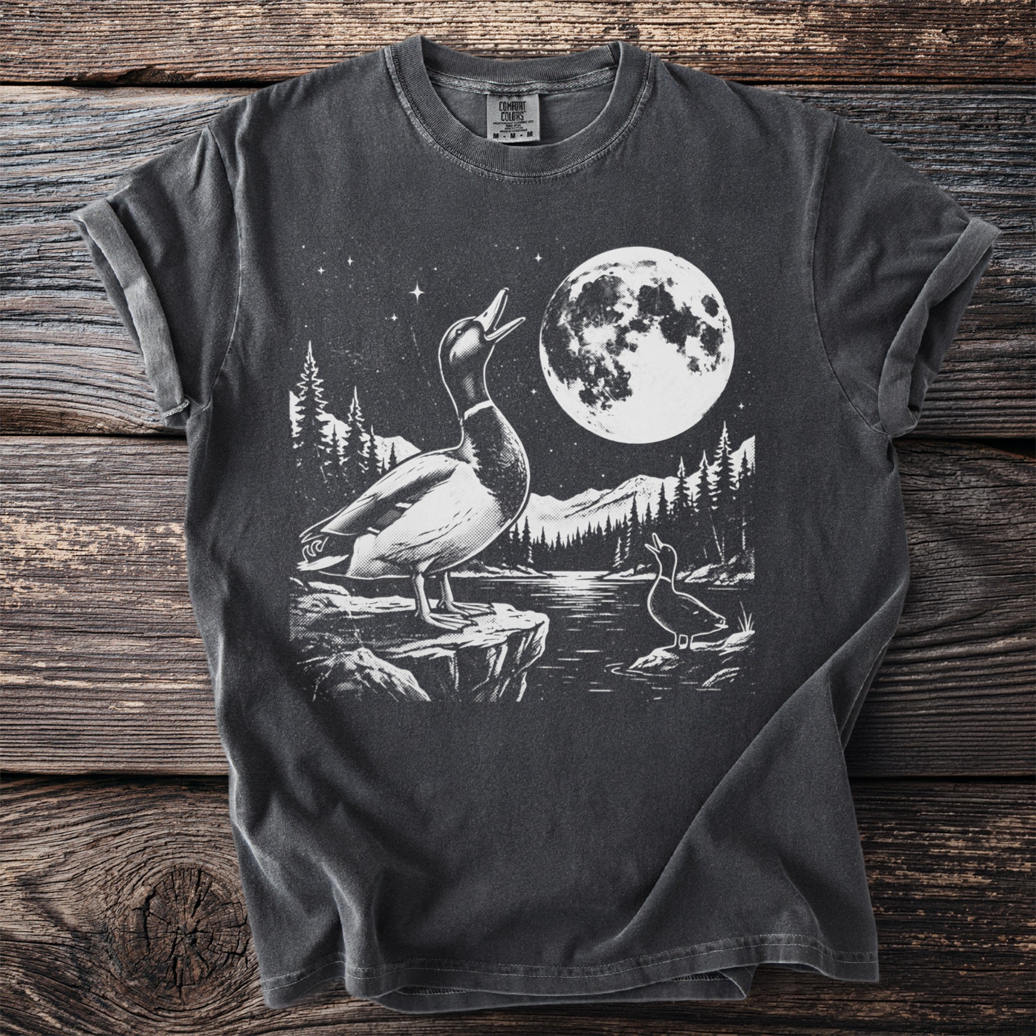 Graphic tee with two ducks and a moon above a starry, mountainous landscape by a lake.