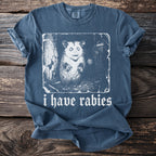 Blue t-shirt with a white graphic of an opossum and the text "i have rabies".