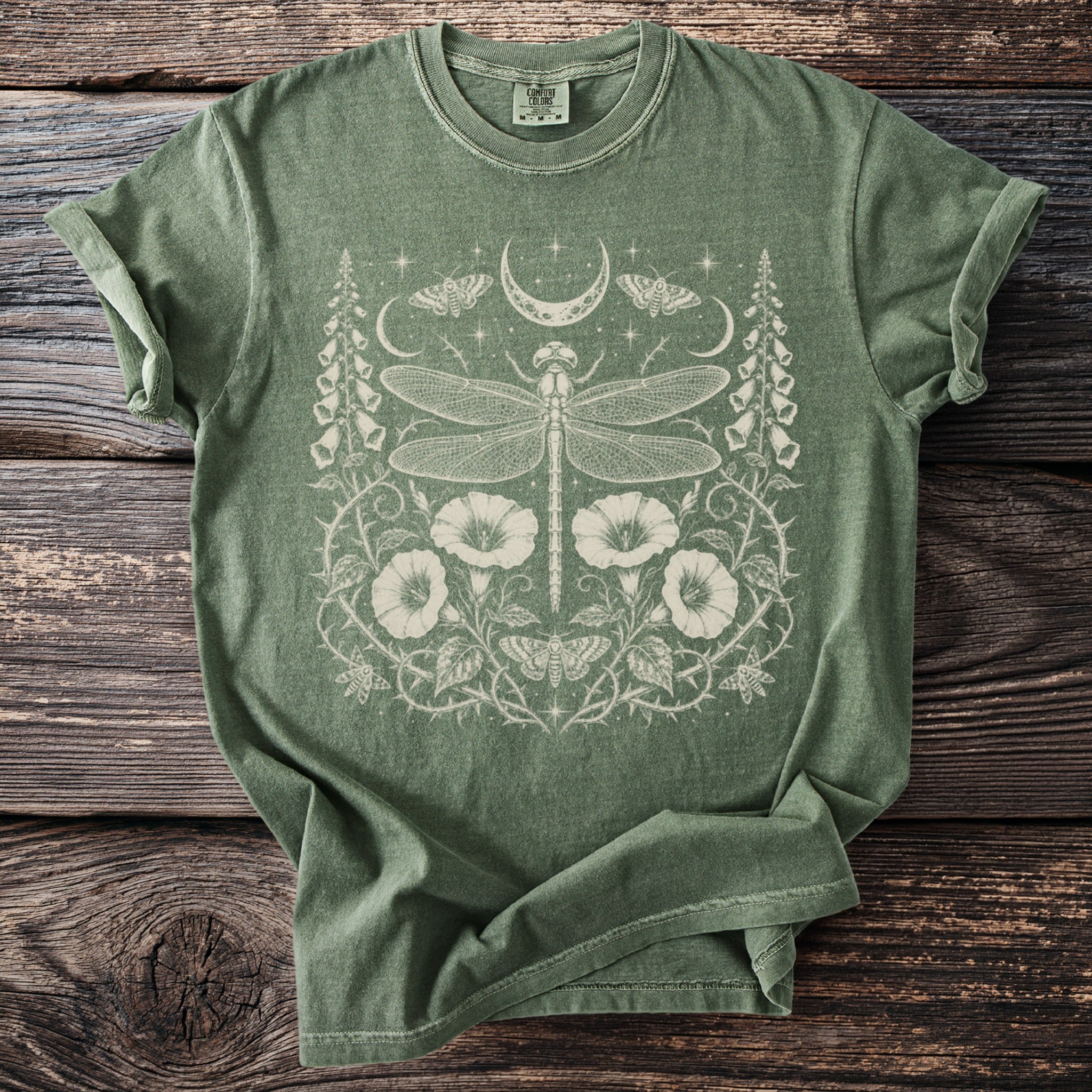 Green t-shirt with a white dragonfly, moon, moth, and floral design.