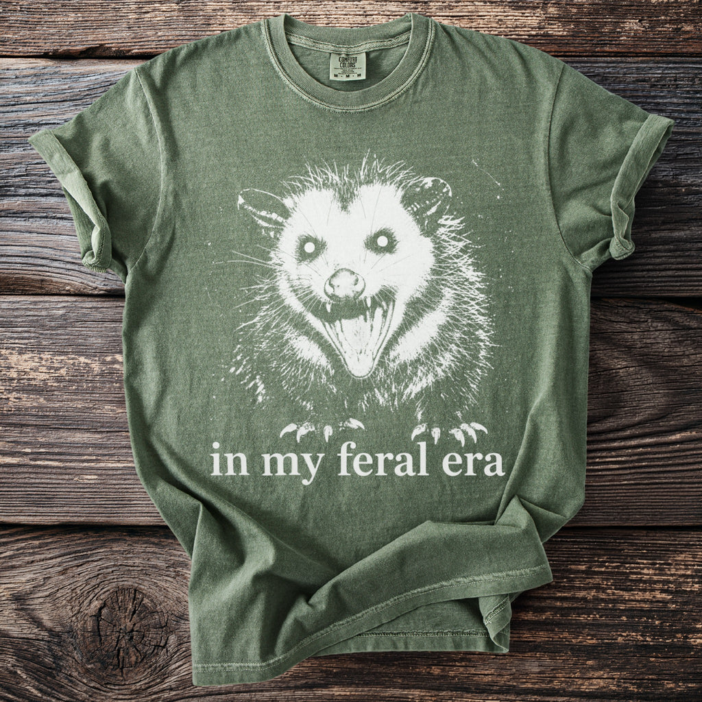 Green t-shirt with white possum graphic and text "in my feral era."