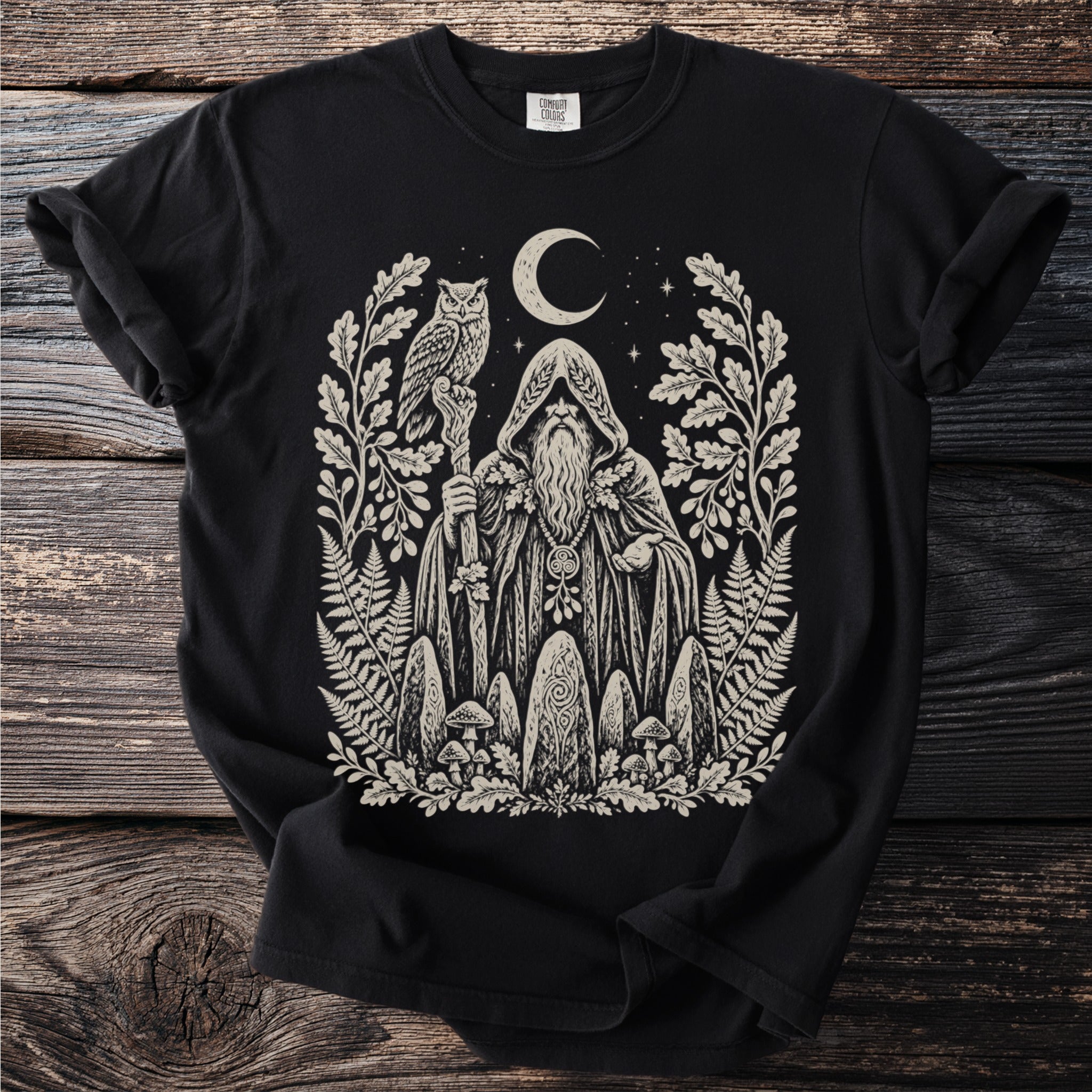 Black t-shirt with a cream linocut print of a wizard holding an owl staff and surrounded by nature.