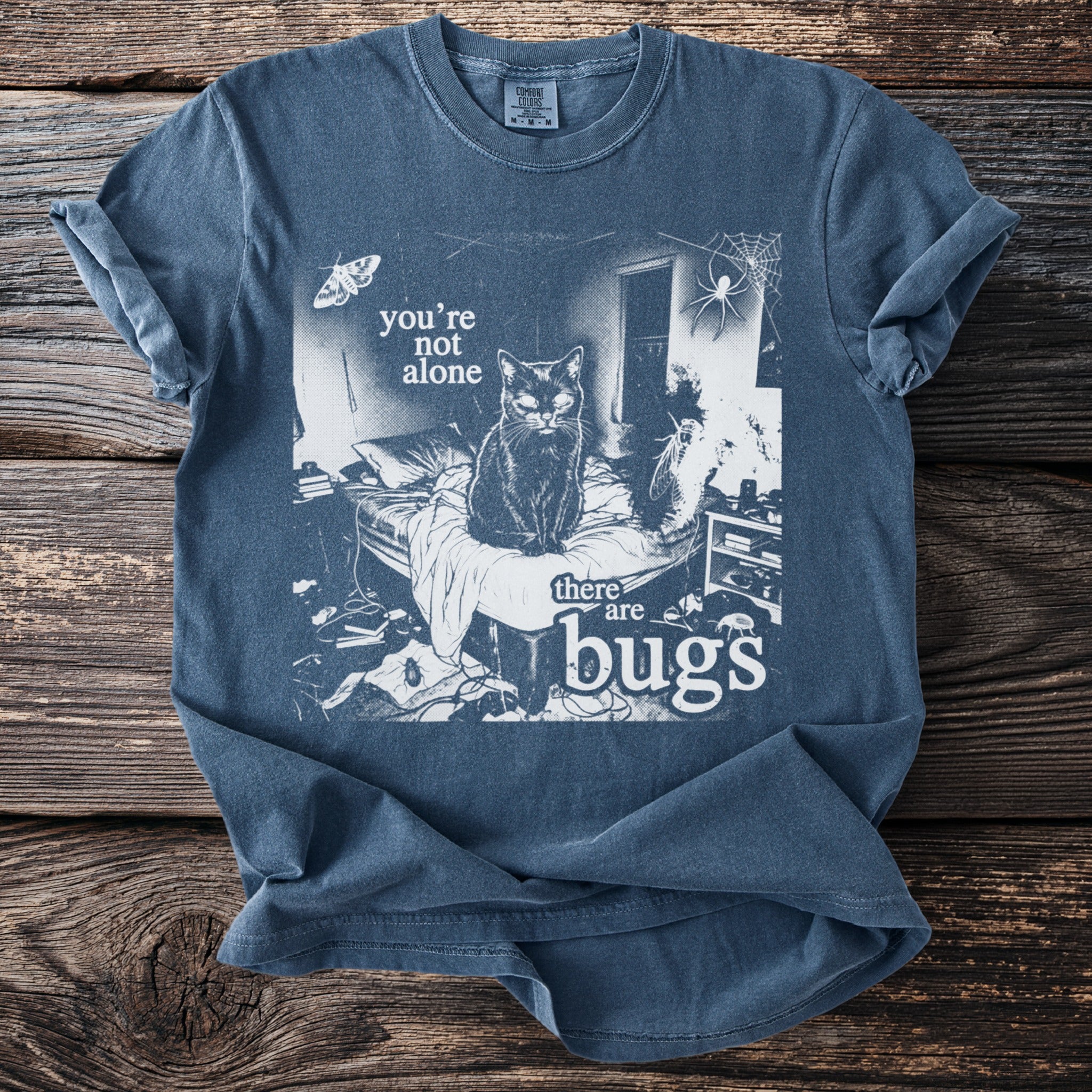 Blue t-shirt with graphic of black cat, moth, spider, and text "you're not alone there are bugs".