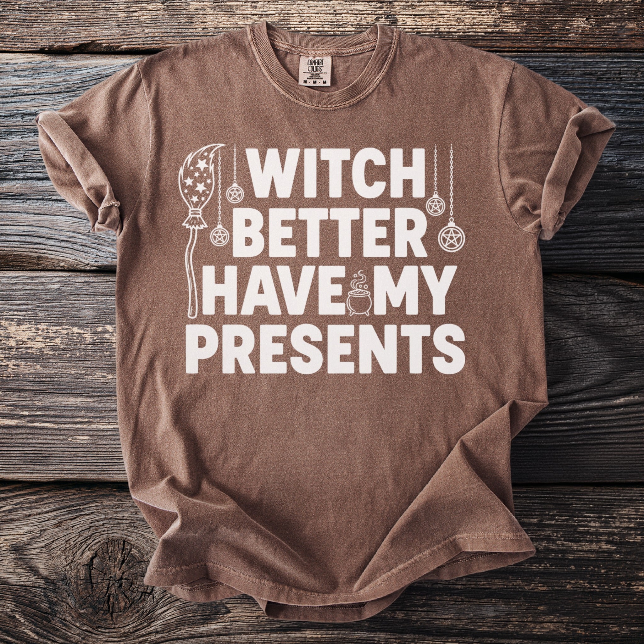 Brown t-shirt with white text "Witch Better Have My Presents" and decorative elements.