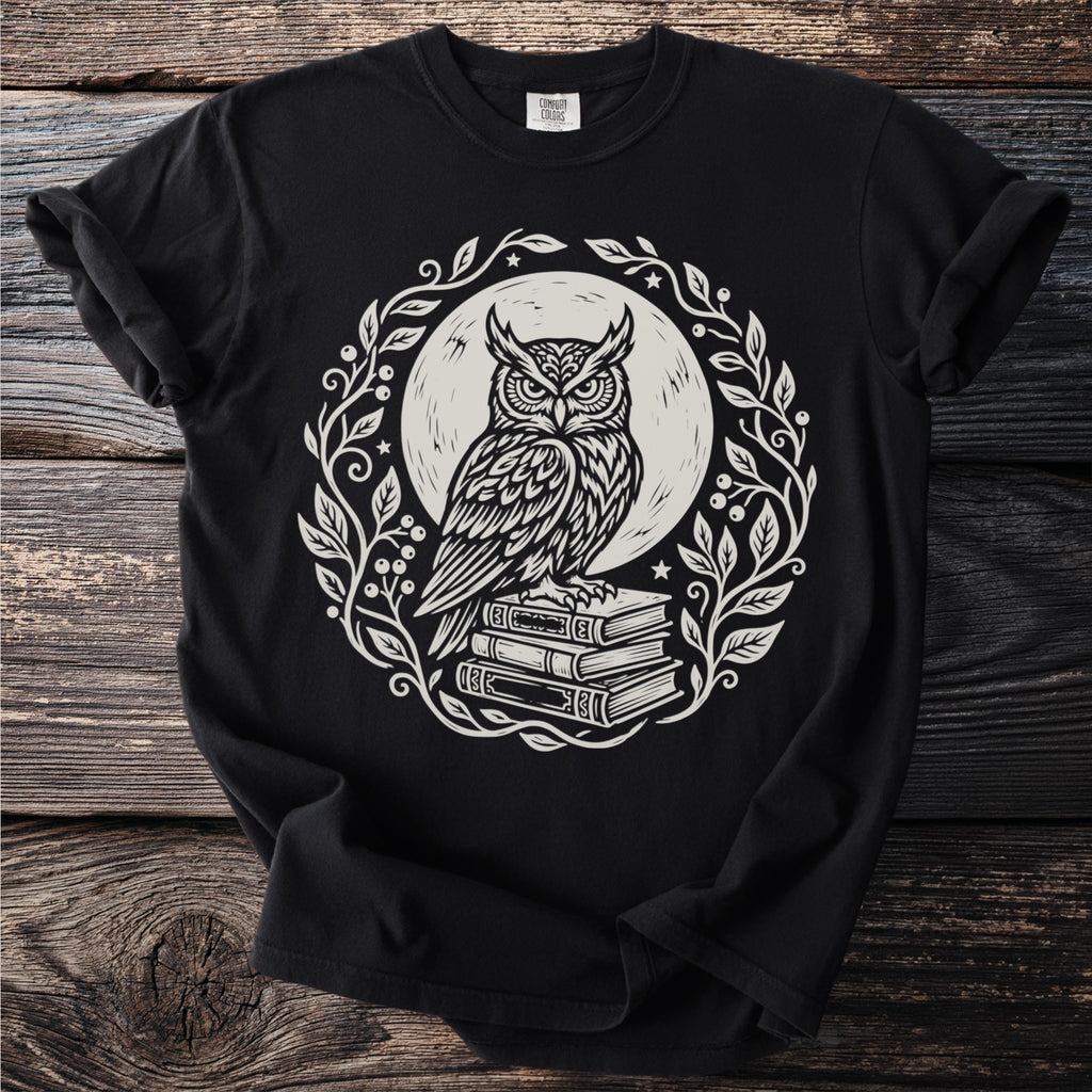 Black t-shirt with white graphic of owl perched on stacked books within a floral wreath.