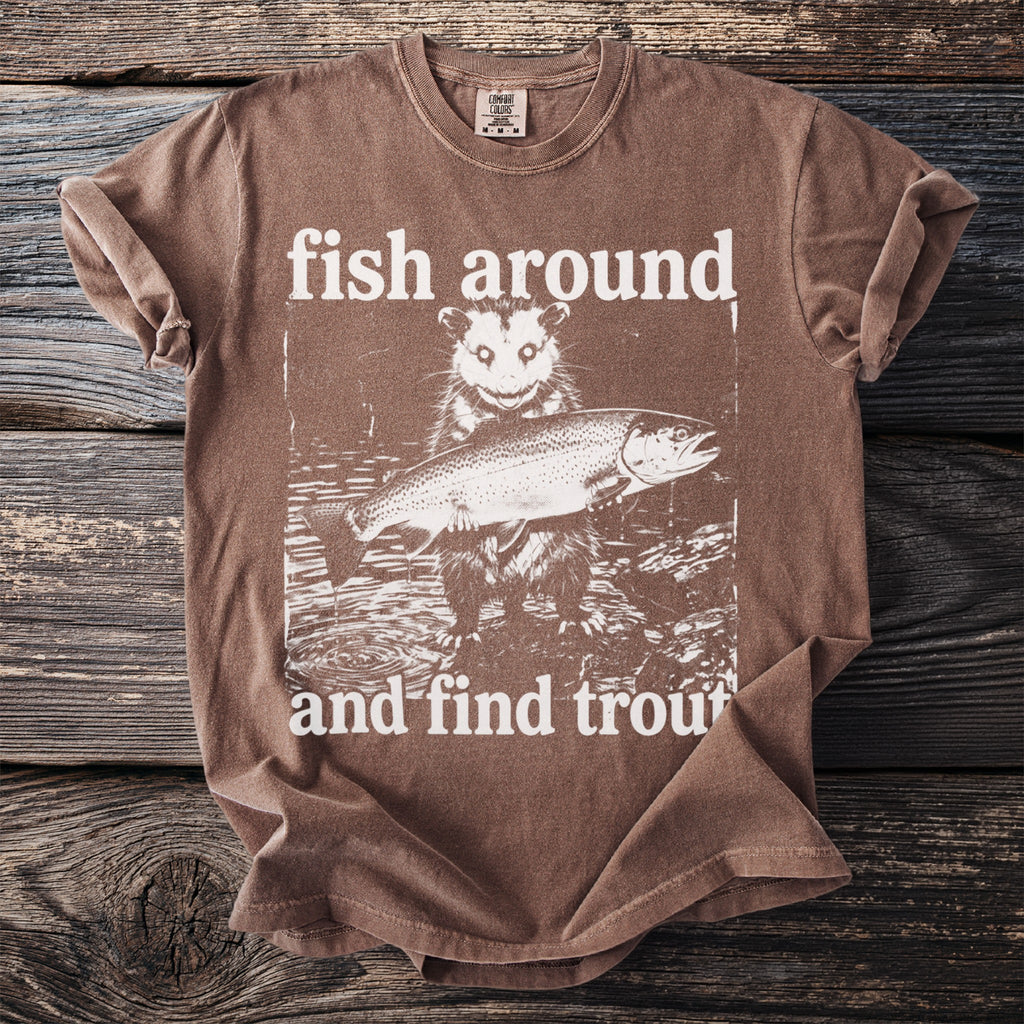 Brown t-shirt with a graphic of an opossum holding a trout and text that reads "fish around and find trout".