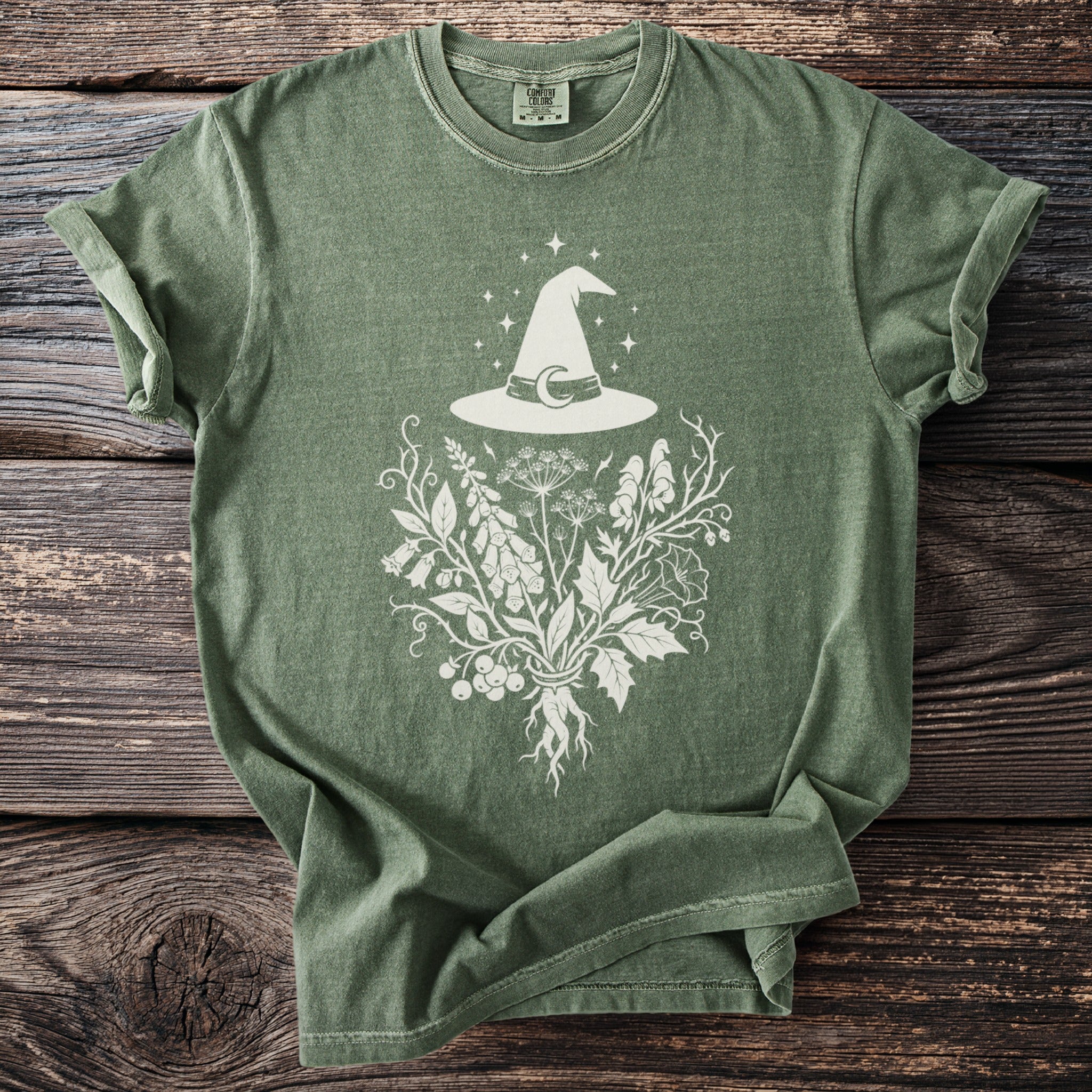 Green t-shirt with white witch hat and botanical graphic.
