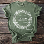 Green t-shirt with white graphic of a thorny wreath containing insects and "Love the Unloved" text.