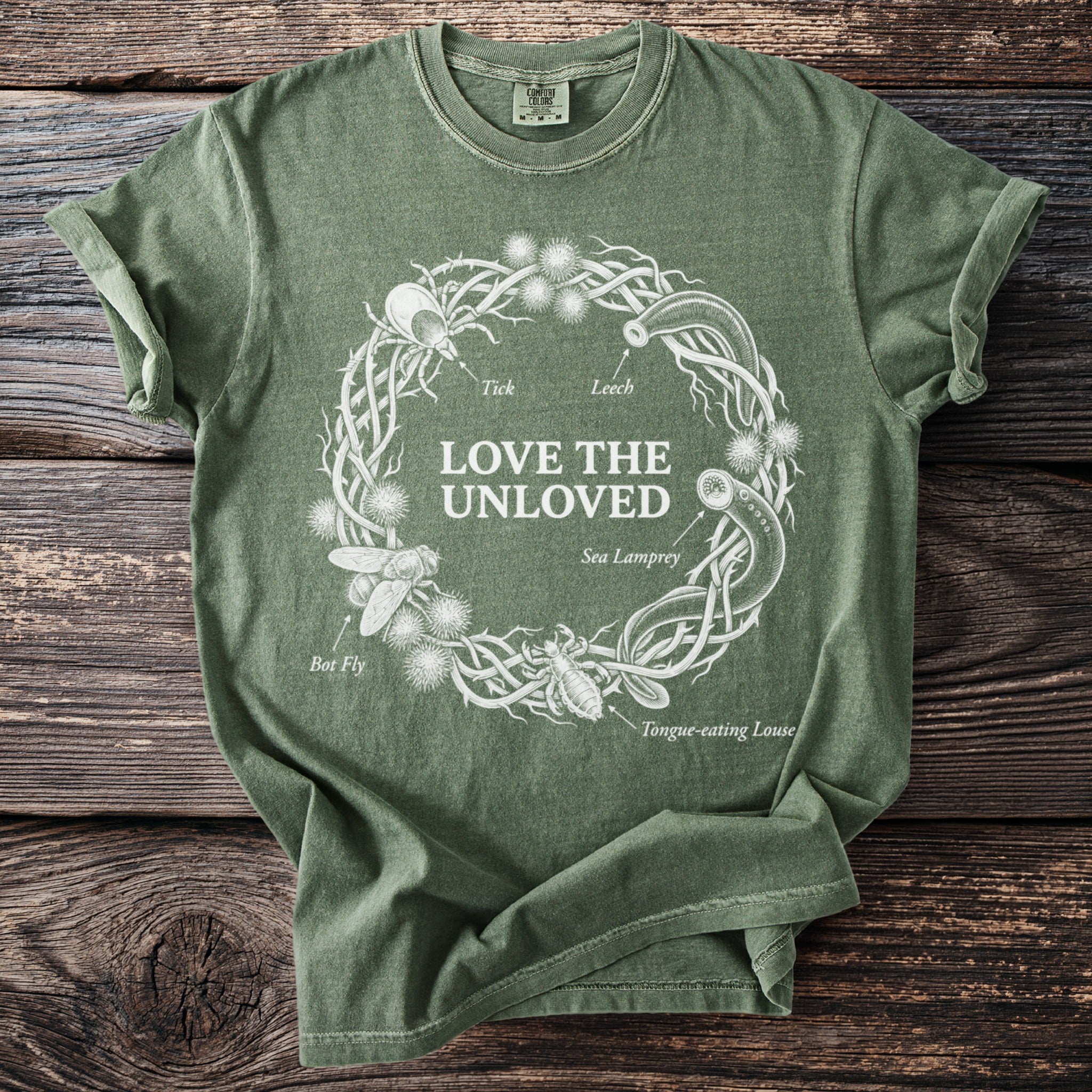 Green t-shirt with white graphic of a thorny wreath containing insects and "Love the Unloved" text.