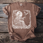Brown t-shirt with white mystical woman spinning thread by a moon and starry sky.