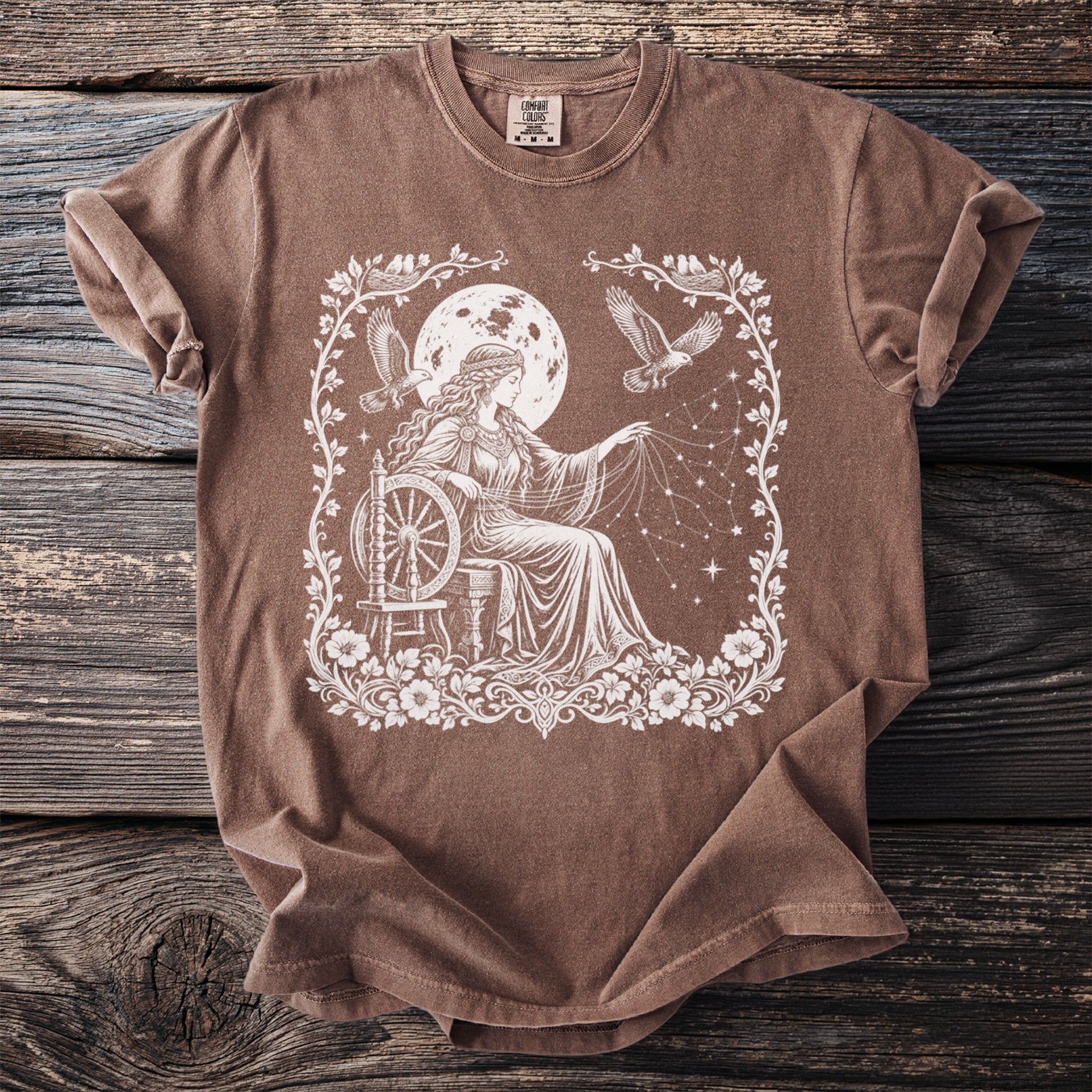 Brown t-shirt with white mystical woman spinning thread by a moon and starry sky.