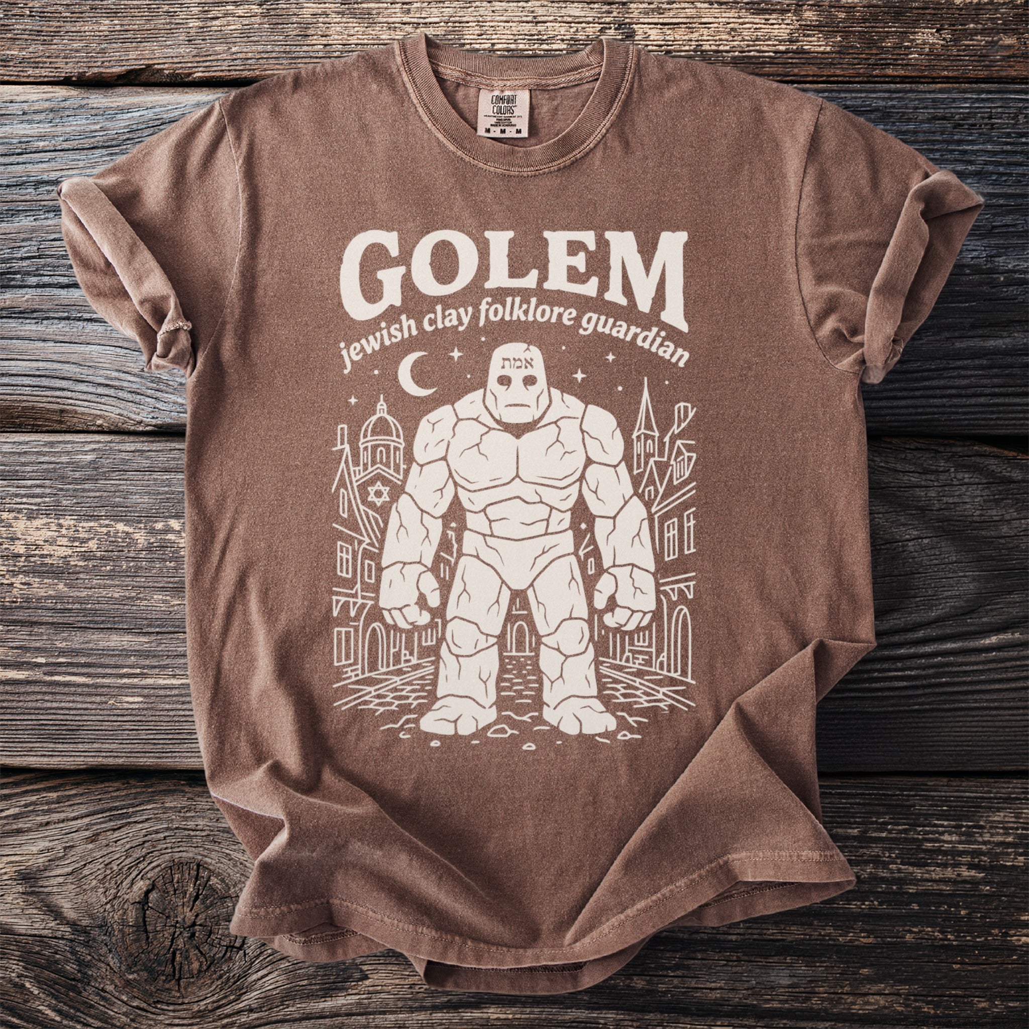 Brown t-shirt with white graphic of a Golem, moon, and city buildings