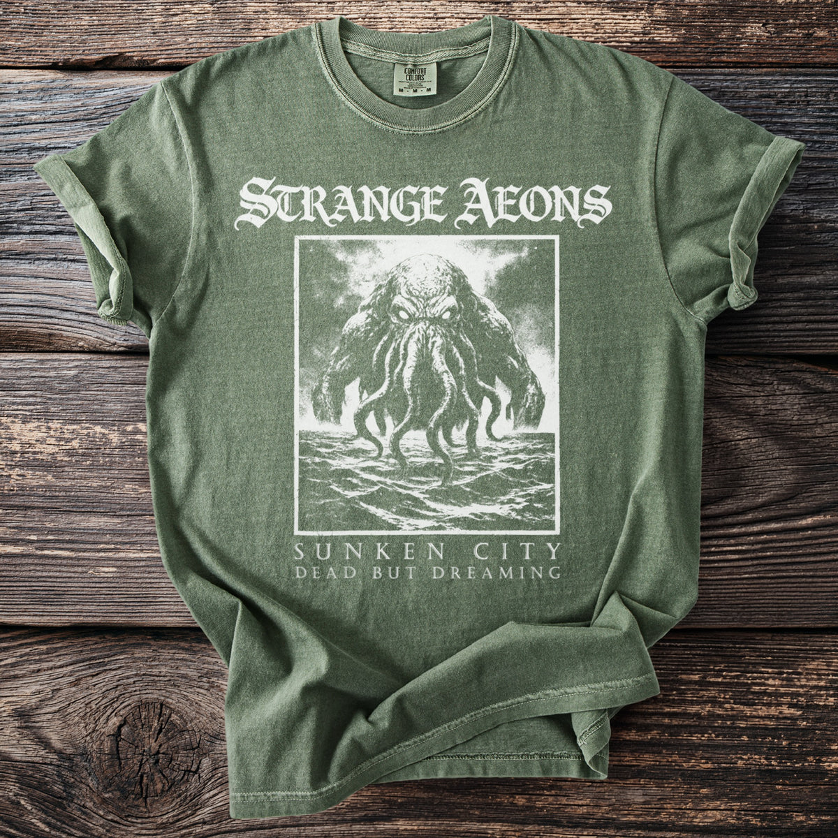 Green t-shirt with a square graphic of a tentacled creature in water and text "STRANGE AEONS SUNKEN CITY DEAD BUT DREAMING".