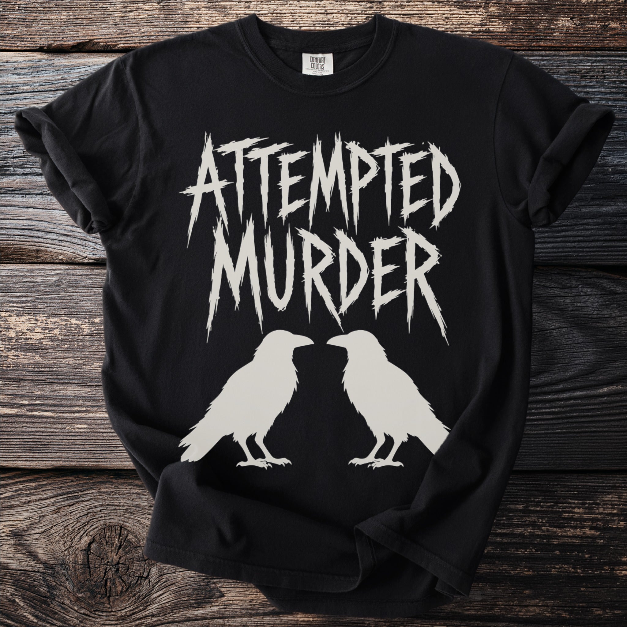 Black t-shirt with white text "ATTEMPTED MURDER" and two white raven silhouettes.