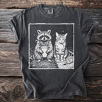 Dark t-shirt with a black and white graphic of a raccoon holding a drink and a cat smoking