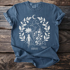 T-shirt with white line art of a witch holding a mandragora and hyoscyamus plants.