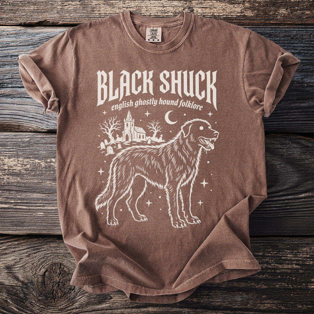 Brown t-shirt with white graphic of a dog, church, and gravestones. Text reads "BLACK SHUCK english ghostly hound folklore."