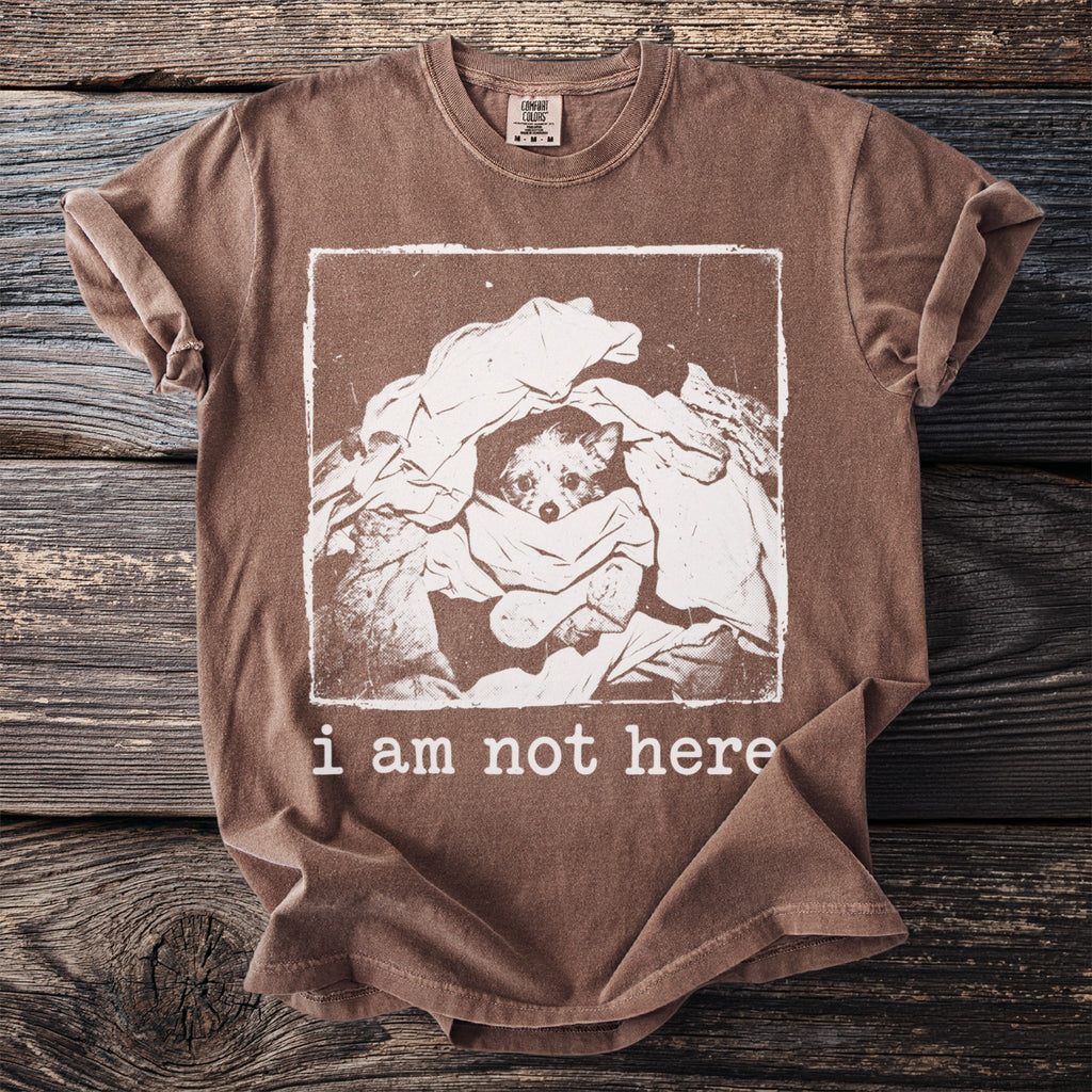 Brown t-shirt with distressed print of a dog peeking out of laundry and text "i am not here".