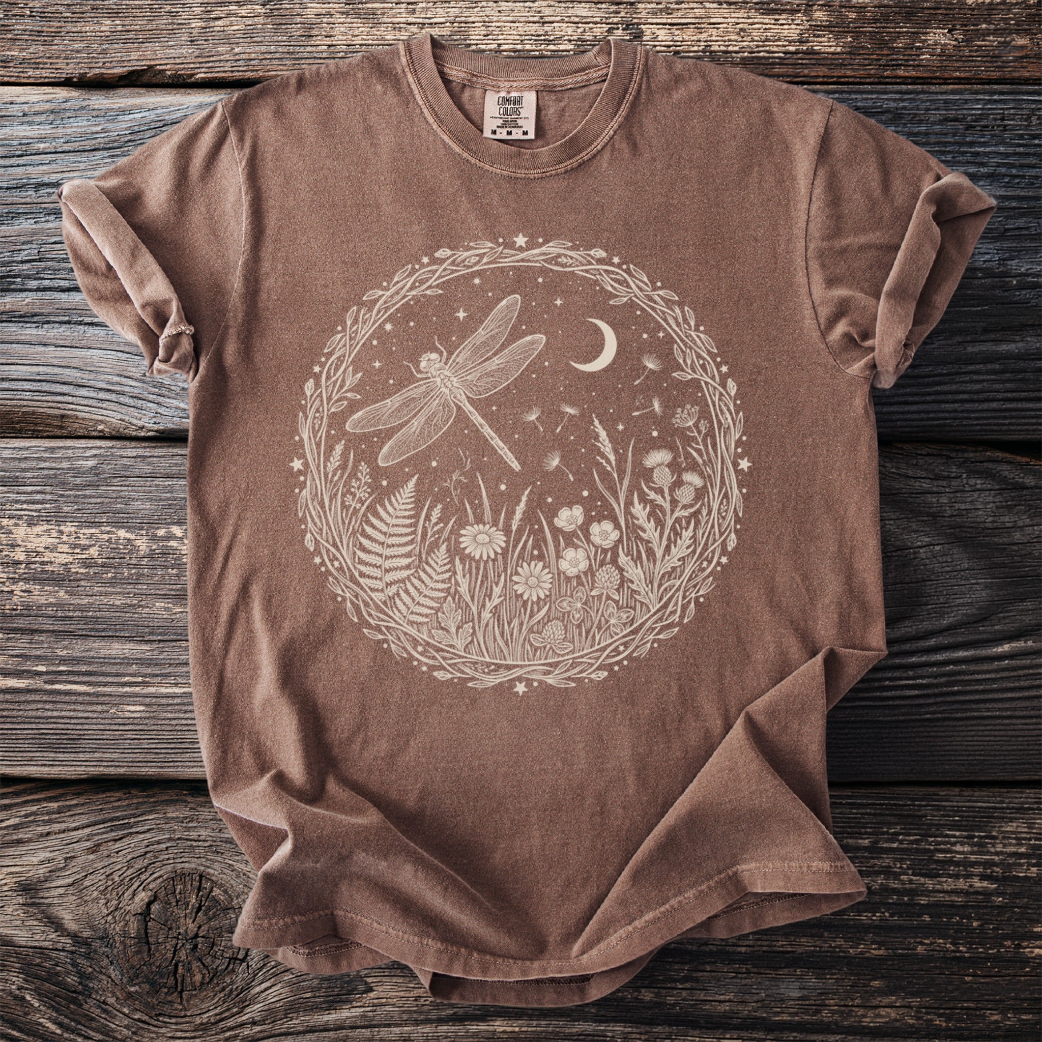Brown t-shirt with a circular white graphic of a dragonfly, moon, and wildflowers.