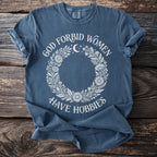 Blue t-shirt with white text and floral wreath graphic: "God Forbid Women Have Hobbies"