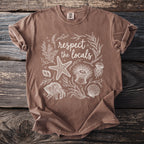 Brown t-shirt with white outline illustration of marine life and text "respect the locals".