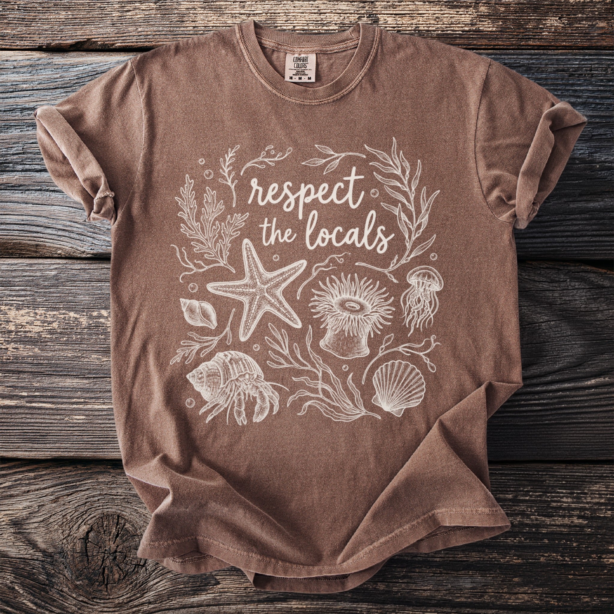 Brown t-shirt with white outline illustration of marine life and text "respect the locals".
