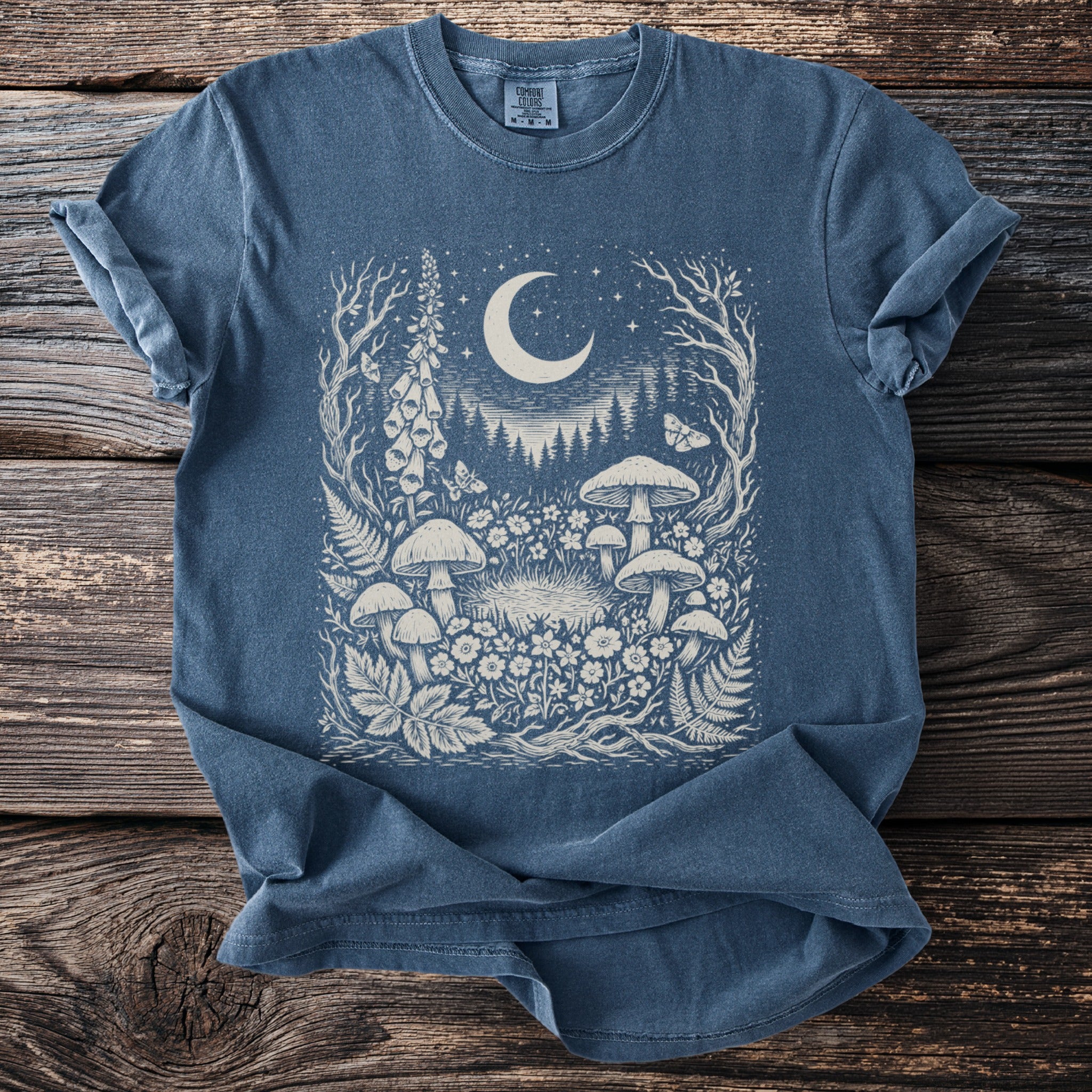 Blue comfort colors t-shirt with white moon, mushrooms, flowers, and moths graphic.