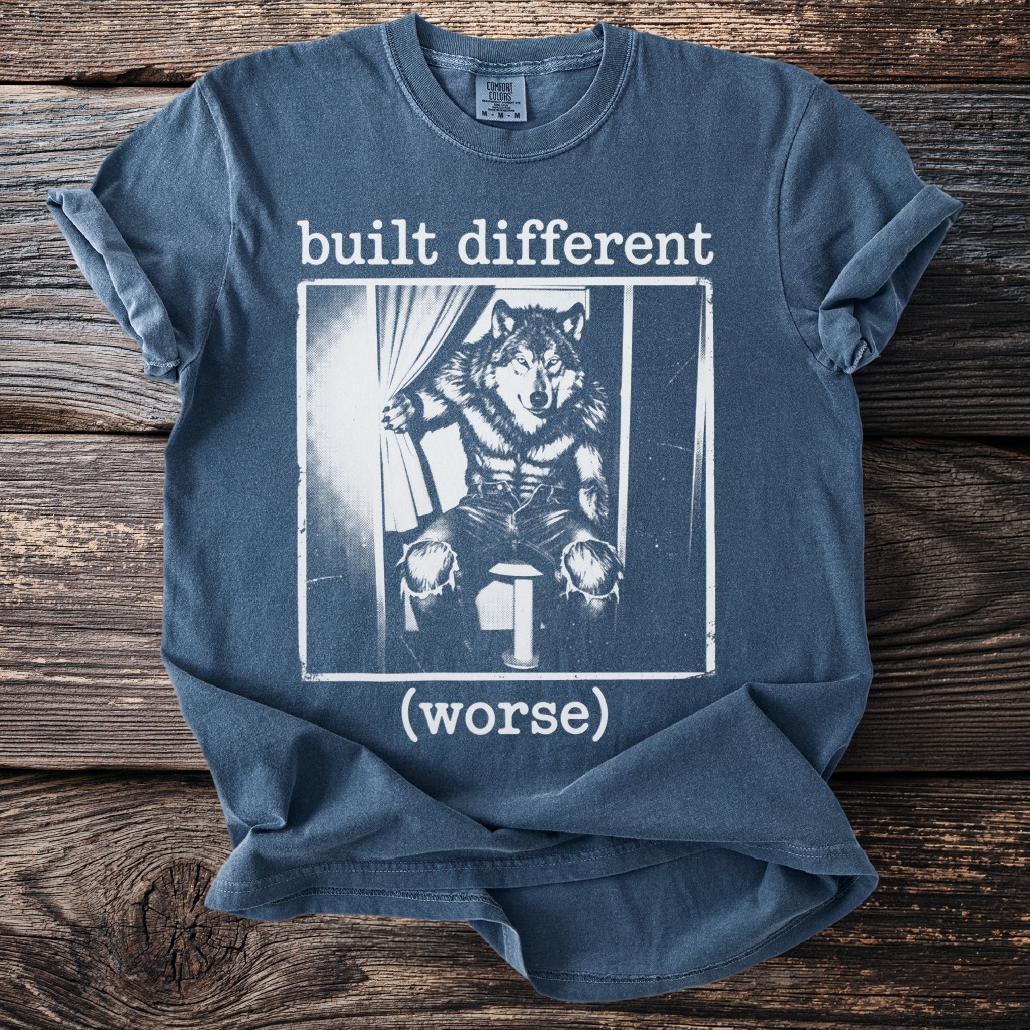 Blue t-shirt with text "built different (worse)" and graphic of a wolf on a stool.
